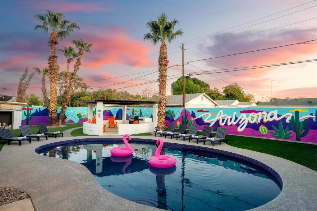 a pool with two pink flamingos in a yard with palm trees at Poolside Paradise Big Backyard Arcade Mural in Mesa