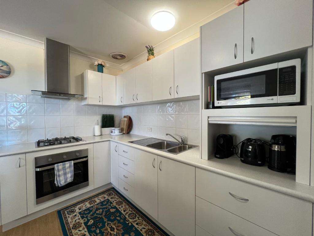 a kitchen with white cabinets and a microwave at Cosy Bayside Studio in Esperance