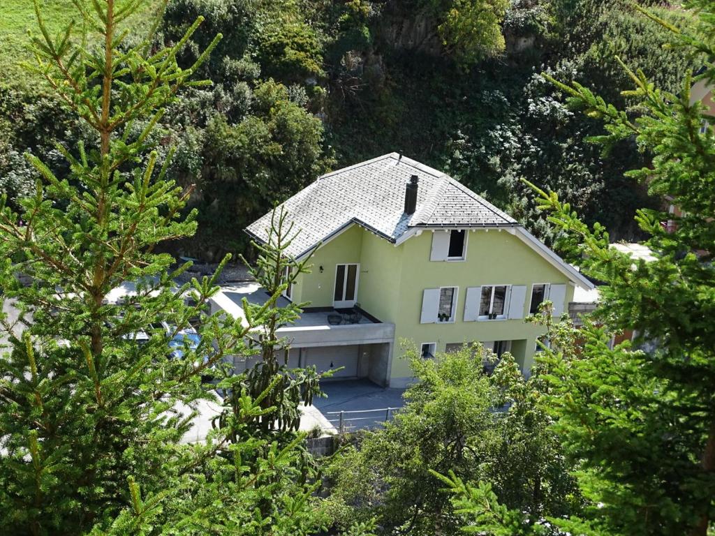 a yellow house is seen through the trees at Ferienhaus Grüner Heinrich in Andermatt