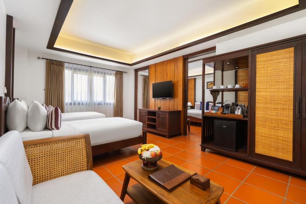 A warm, traditional-style guest room with a large bed, sofa, television and drinks station.