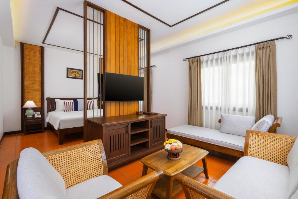 A bright sitting room with rattan seating, a television and a bedroom glimpsed behind a partition.
