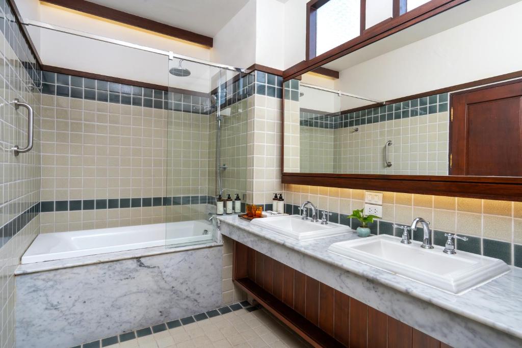 A bright bathroom with twin sinks, a bathtub and a separate glass-enclosed shower.