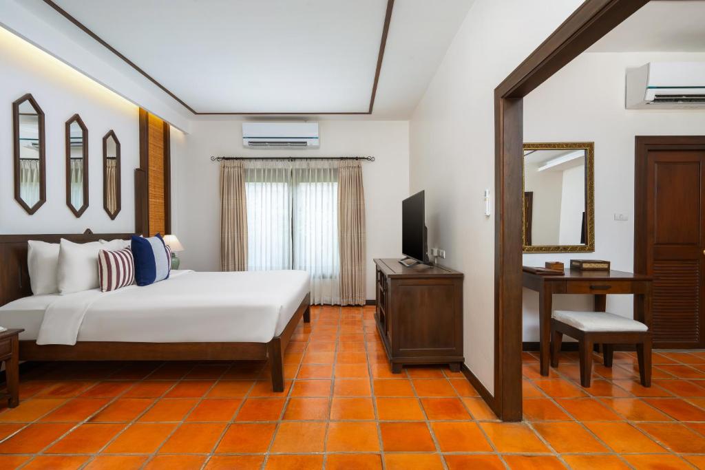 A bedroom with a large bed, television, air conditioner and a separate dressing desk.