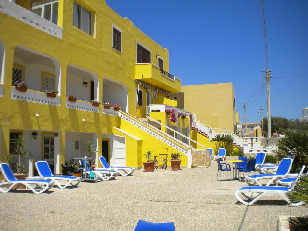 um edifício amarelo com espreguiçadeiras azuis em frente em Hotel Mare Blu em Lampedusa