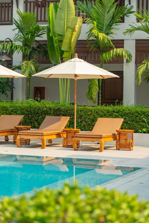 A poolside row of wooden loungers under a cream umbrella beside tropical planting.