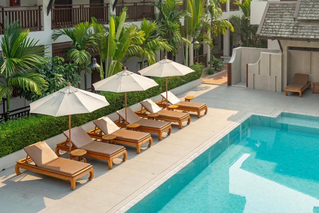 A bright rectangular pool lined with loungers and umbrellas in a planted courtyard.