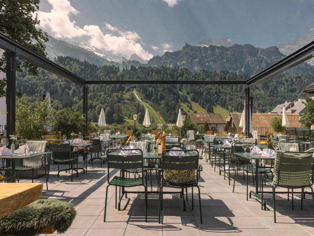 a patio with tables and chairs with mountains in the background at Alpenclub in Engelberg