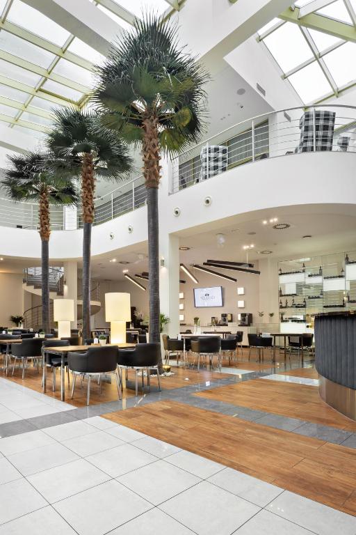 a lobby with palm trees and tables and chairs at Hotel Moderno Poznań in Poznań