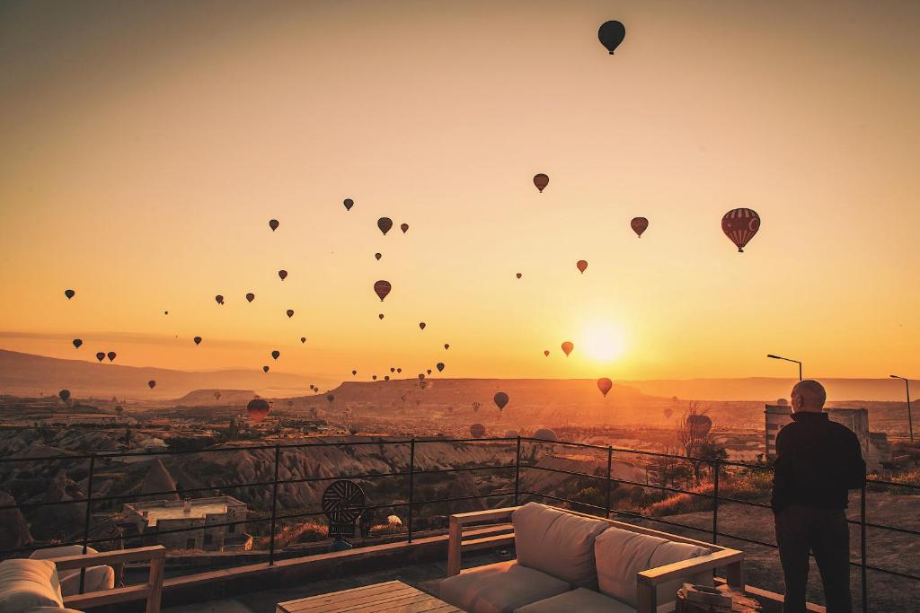 a man standing on a balcony watching hot air balloons at Millstone Cave Suites Hotel in Uçhisar