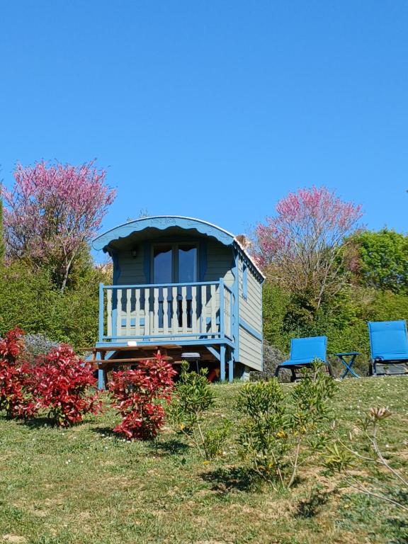a small house with two blue chairs in the grass at Roulotte du Touton avec climatisation in Preignan