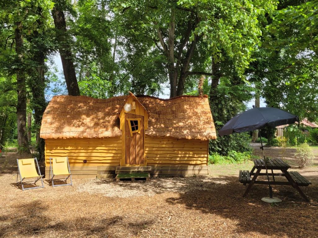 a small log cabin with chairs and an umbrella at Cabane Magique 4 Personnes in La Bâtie-Montgascon
