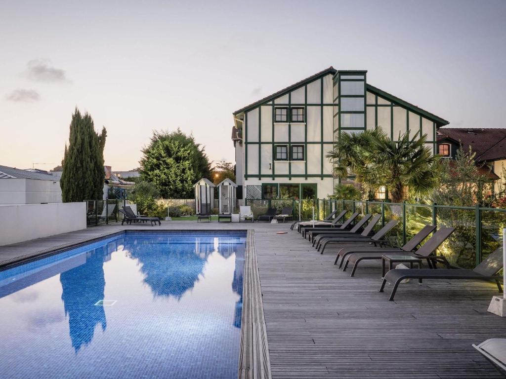 a house with a swimming pool with chairs and a building at ibis Styles Saint-Jean-de-Luz Donibane in Saint-Jean-de-Luz