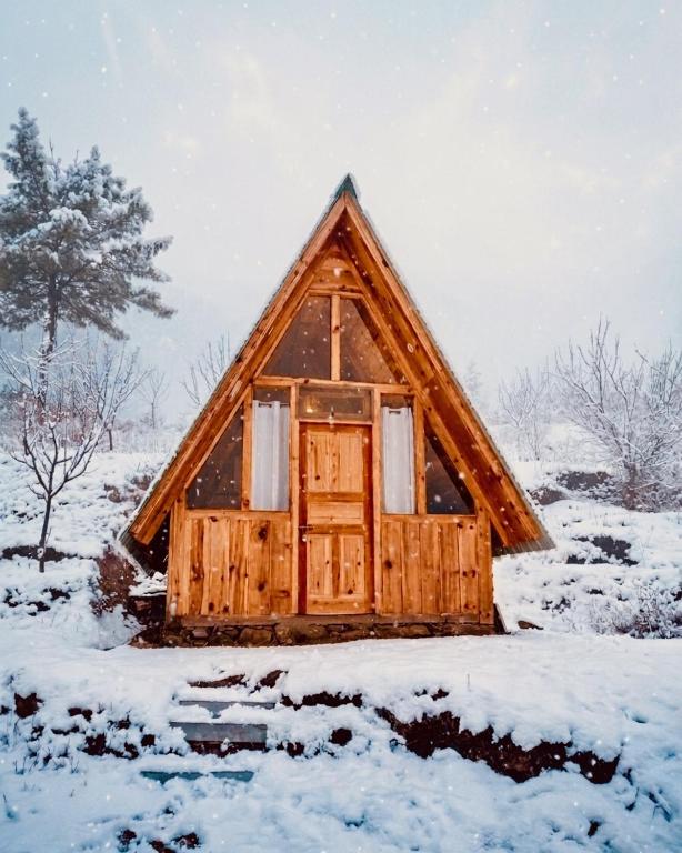 a wooden cabin with a door in a snow covered field at Hima 360, A Frame Cabin, Panaromic Sainj Valley Views, Bhatkanda in Sainj