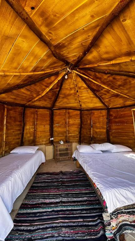 two beds in a large wooden room with a rug at Fayoum Desert Camp in Qaryat Ḩātim aţ Ţāʼī