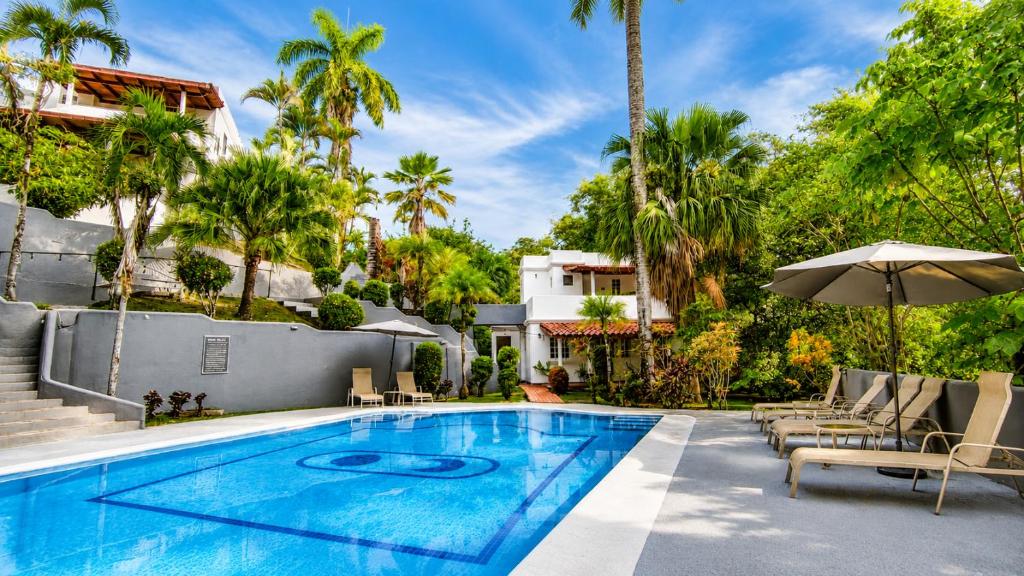 a swimming pool with chairs and an umbrella next to a house at Alma Vida Hotel in Manuel Antonio