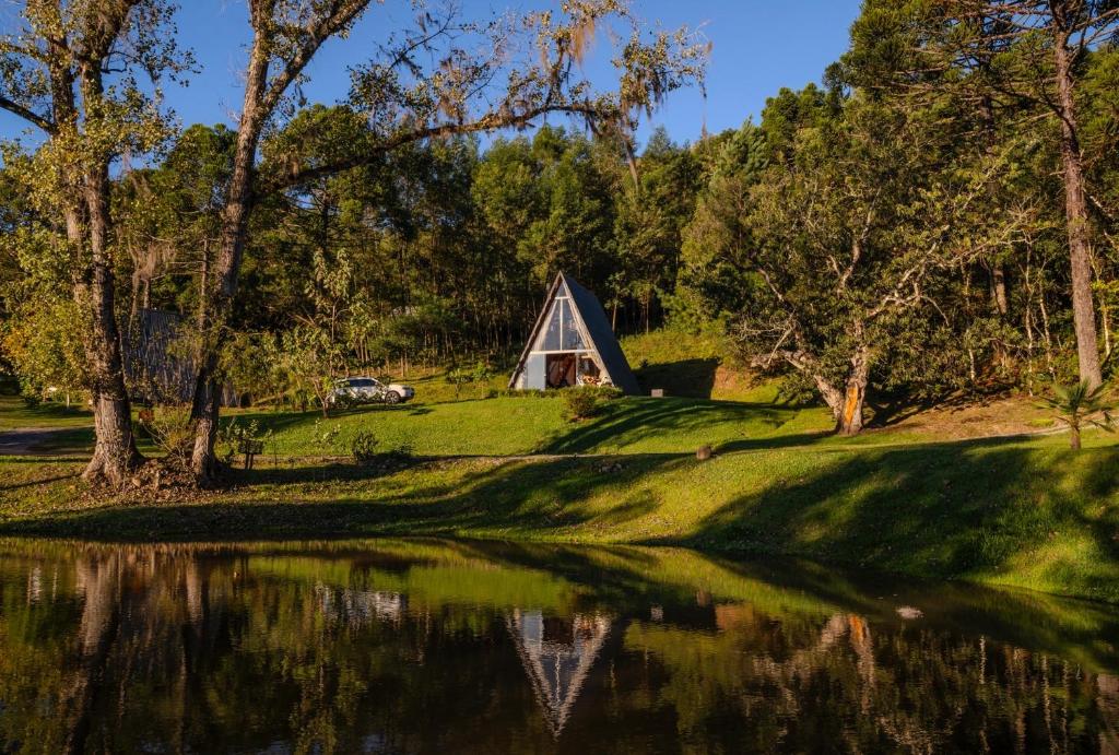 a cabin next to a lake with trees at Cabana com banheira in Gramado