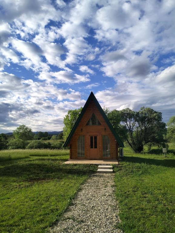 a small cabin in a field with a cloudy sky at RIVERSTONE Drašković camp and bungalows in Nikšić
