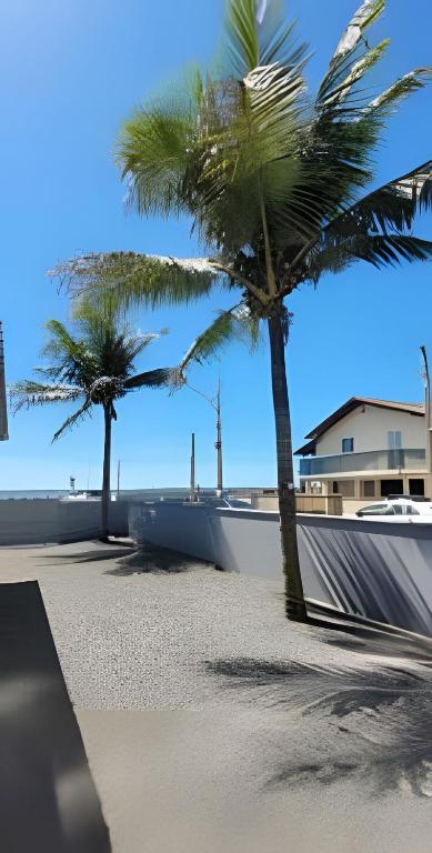 two palm trees on a beach with a building at Refúgio ensolarado a poucos passos do mar in Navegantes