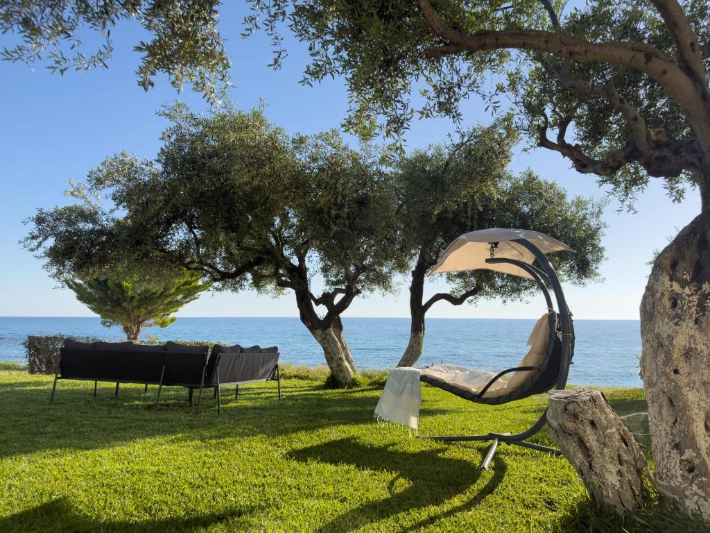 a chair under a tree next to the ocean at Blue Residences in Paralia Vrachou