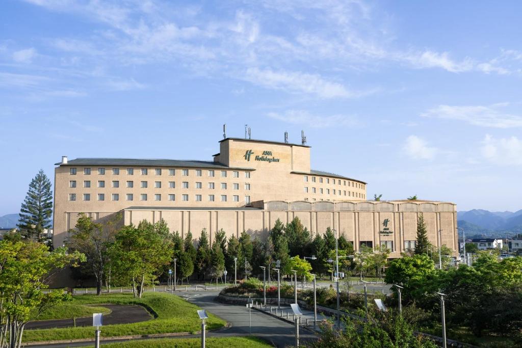 a large tan building with a sign on it at ANA Holiday Inn Kobe Sanda by IHG in Sanda