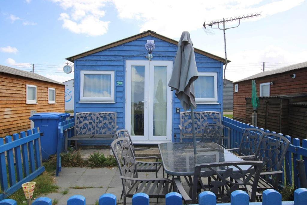 a blue house with a table and chairs and an umbrella at Sheppey Village Ollie in Leysdown-on-Sea