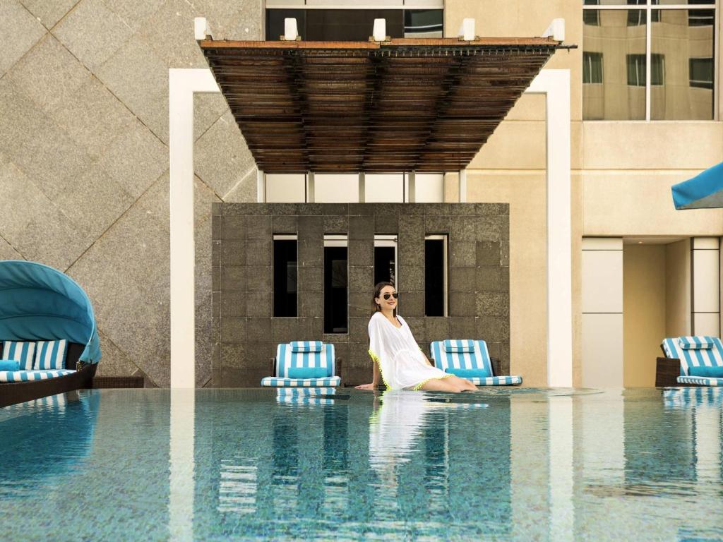 a woman sitting on chairs in a swimming pool at Novotel Deira Creekside Dubai in Dubai