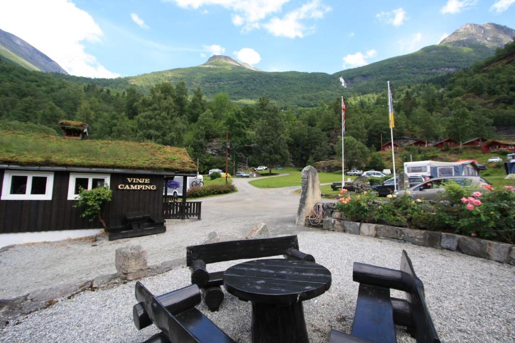 a table and benches in front of a building with mountains at Vinje Camping in Geiranger