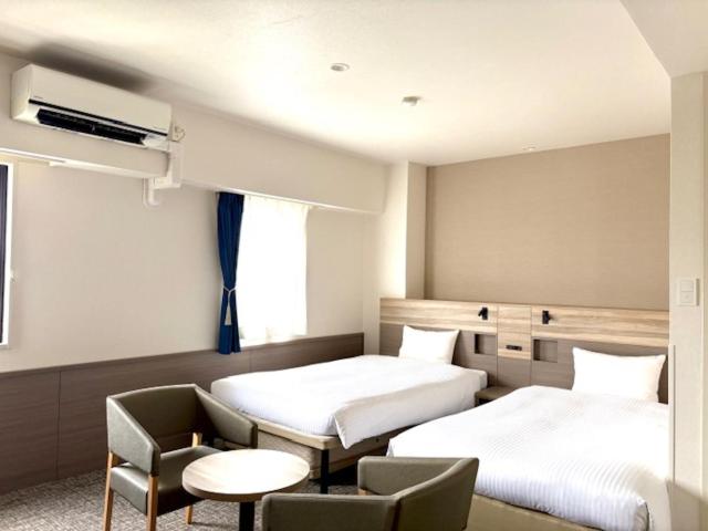 a hotel room with two beds and a chair at Smile Hotel Kitaasaka in Asaka
