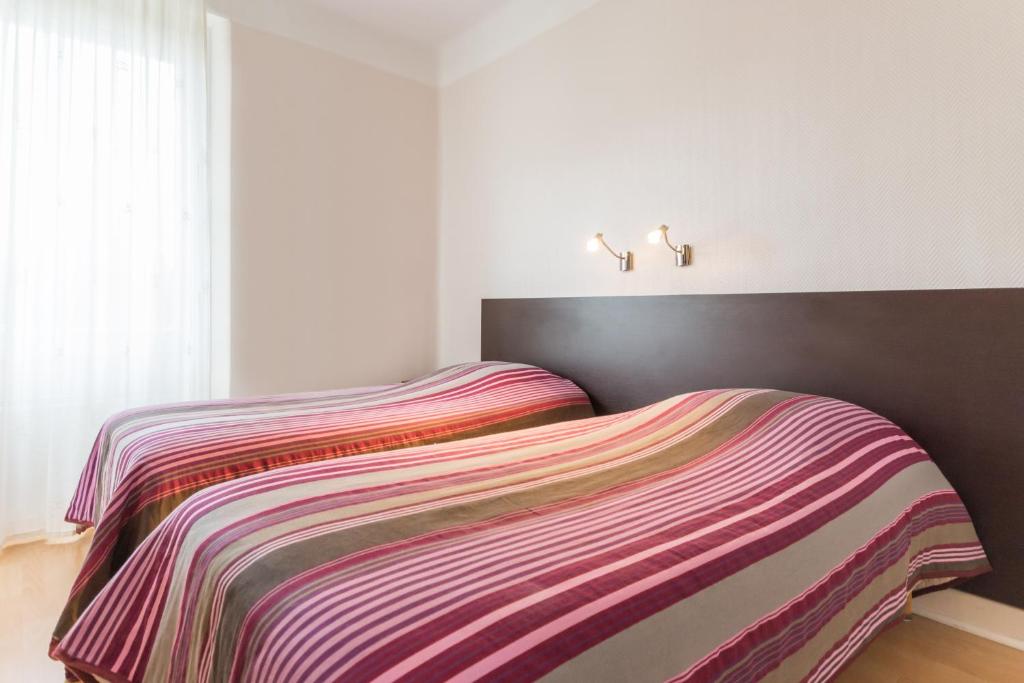 a bedroom with a bed with a striped blanket at Logis Hôtel Le Jabron in La Bégude-de-Mazenc