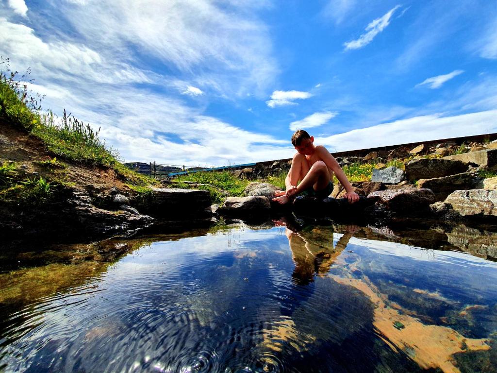 a shirtless man sitting on rocks near a stream at Hótel Laugarhóll with natural hot spring in Laugarholl