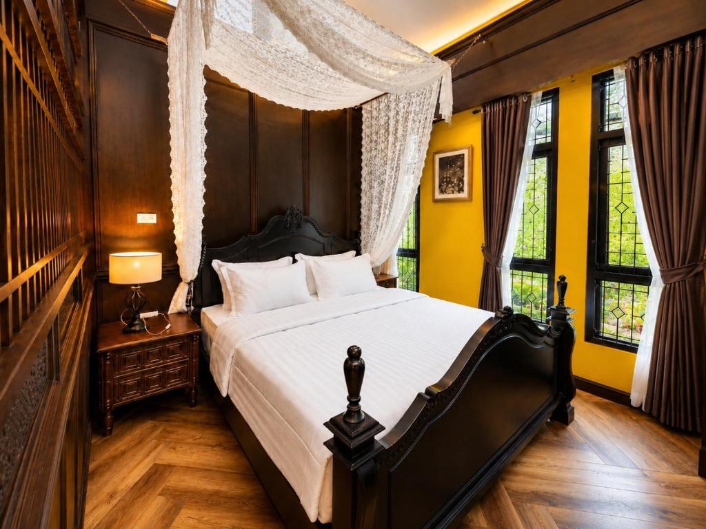 a bedroom with a large bed with yellow walls and windows at Baannaisuk Pool Villa in Ban Mae Pu Kha