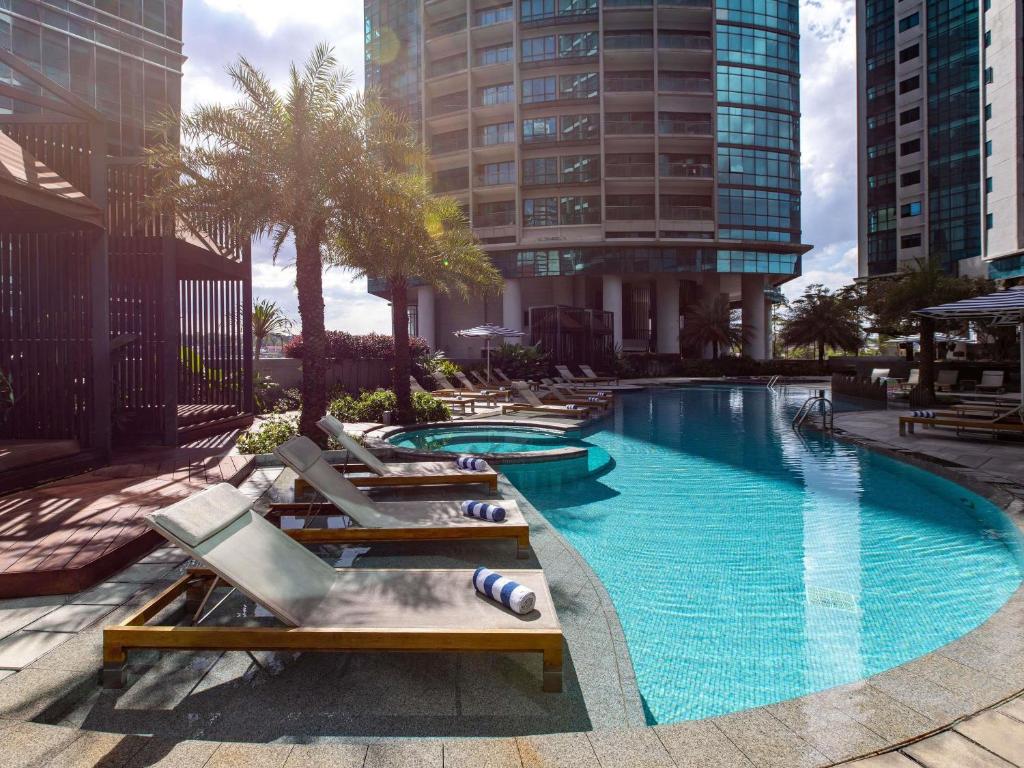 A curving outdoor pool deck surrounded by loungers, palms and city towers.