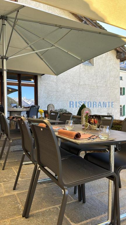 a table with chairs and an umbrella on a patio at Hotel Stüa Granda in Soglio