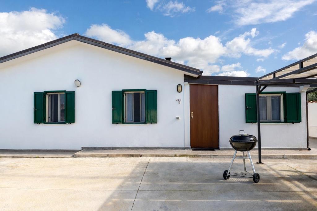 a white house with green shuttered windows and a grill at Villa Claudia - Appartamento B in Corazzello