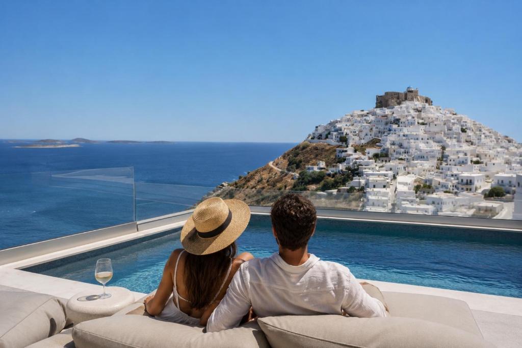 a man and woman sitting on a couch in front of a view of a city at GrandeMar Suites in Astypalaia