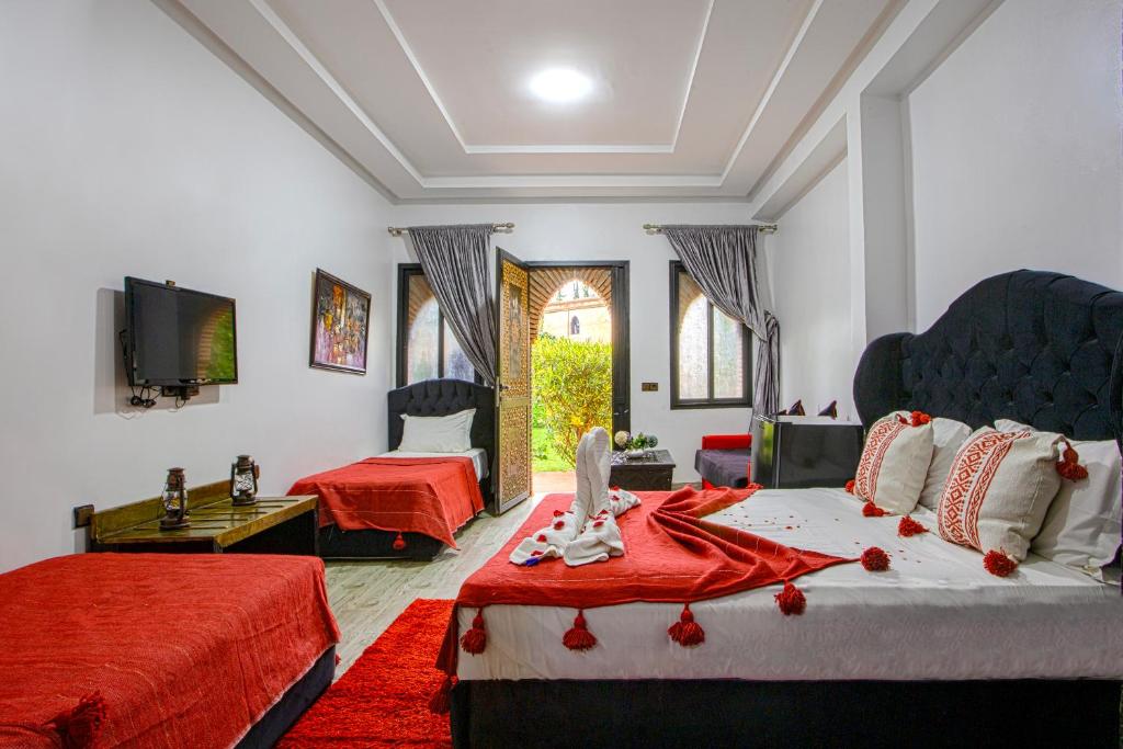 a bedroom with two beds with red sheets and a tv at Domaine Ghait in Had Abdallah Rhiat