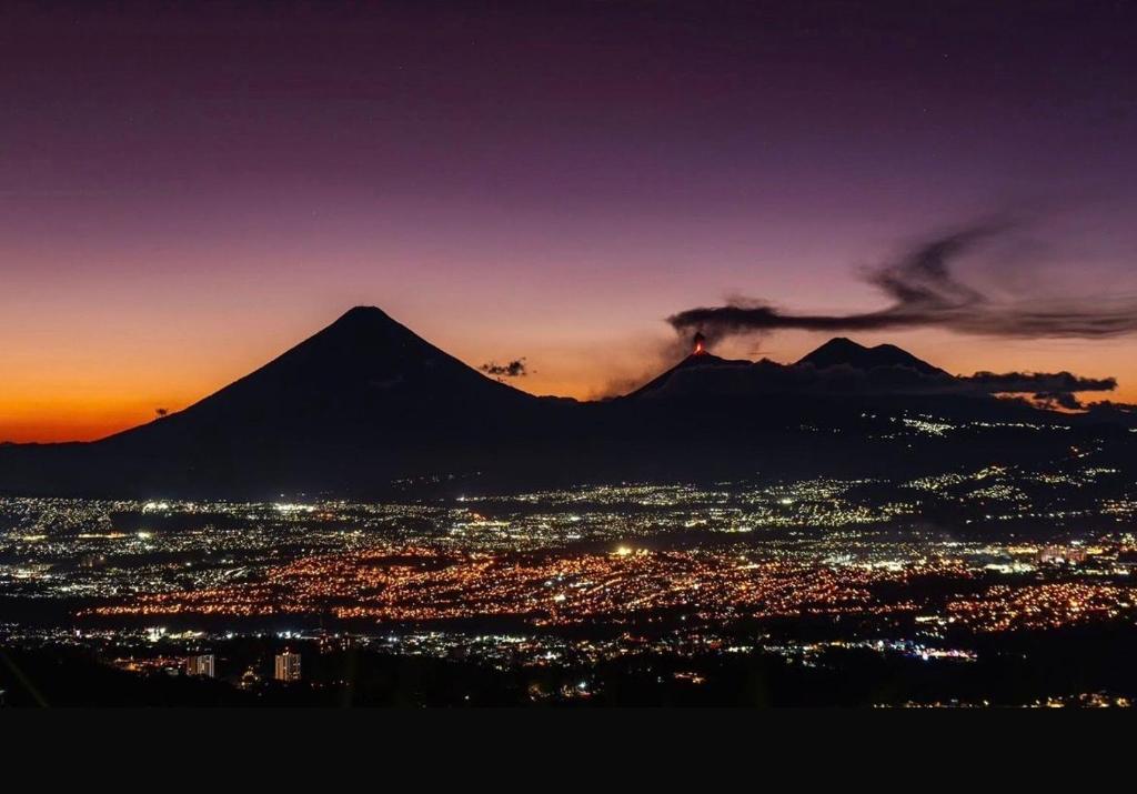 a view of a mountain with a city at sunset at Escápate-Room gt A 15 minutos del aereopuerto transporte gratis vista a los volcanes in Guatemala