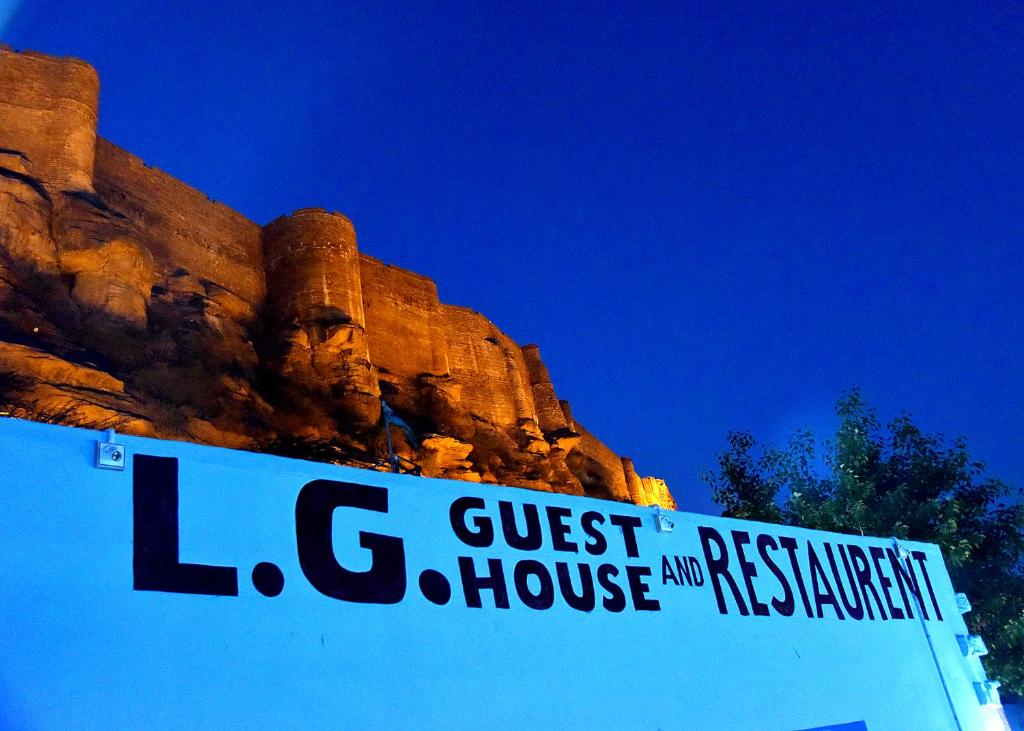 un cartel que lee la casa de huéspedes y el restaurante al lado de una montaña en L G Guest House, en Jodhpur