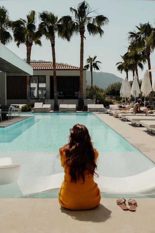 a woman sitting in front of a swimming pool at Insulae Resort in Cefalù