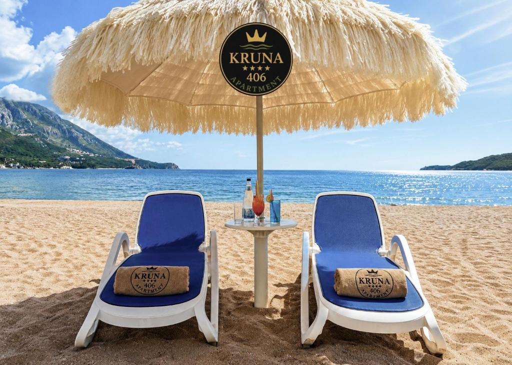 two chairs and a table under an umbrella on the beach at KRUNA 406 Luxury Sea View Apartment with Parking, Minibar, Spa & Beach - Includes 2 Complimentary Non-Alcoholic Beach Drinks & Welcome Gift in Budva