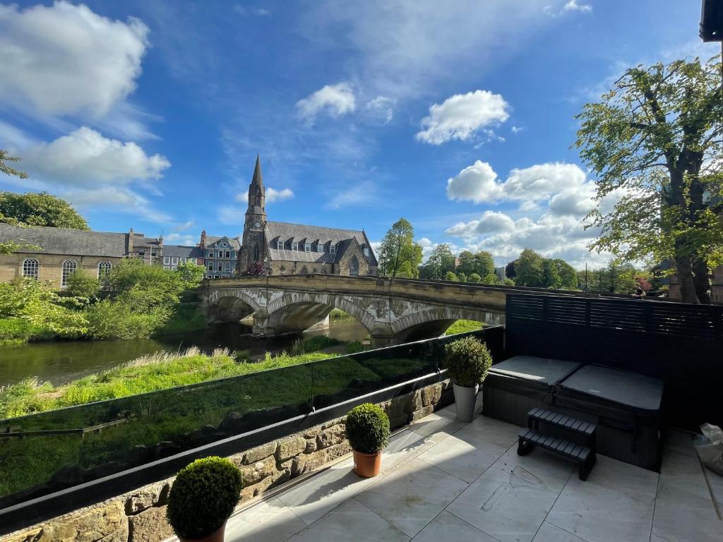 a bench next to a river with a bridge at Riverside Stay in Morpeth