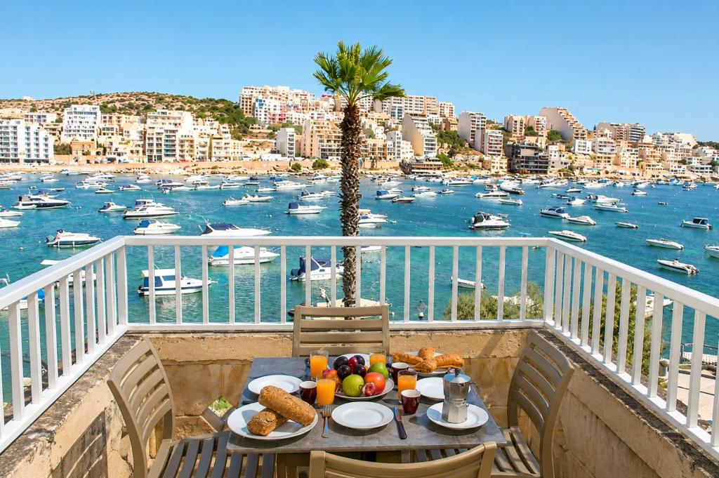 a table with food on a balcony with a view of a harbor at Blue Harbour 2 bedroom Seafront Apartments with large terrace with spectacular sea views - by Getawaysmalta in St. Paul's Bay
