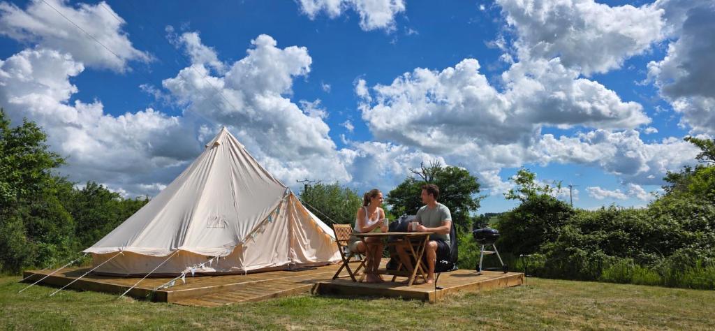 a man and woman sitting at a table in front of a tent at Camping le Monteil in Évaux-les-Bains