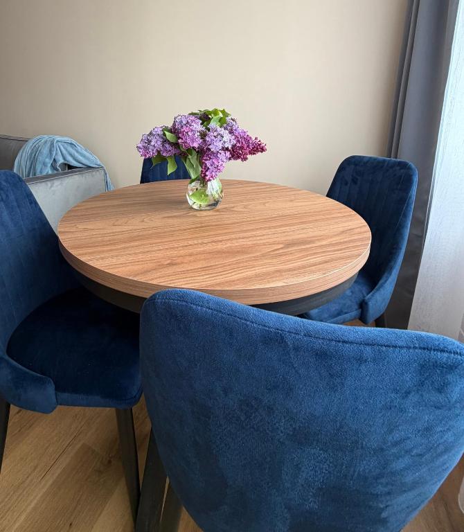 a wooden table with blue chairs and a vase of flowers at MG Apartament City Park in Szczecinek
