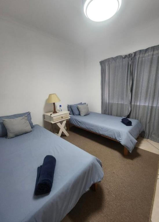a bedroom with two beds and a table with a lamp at Sea side cottage in Stilbaai