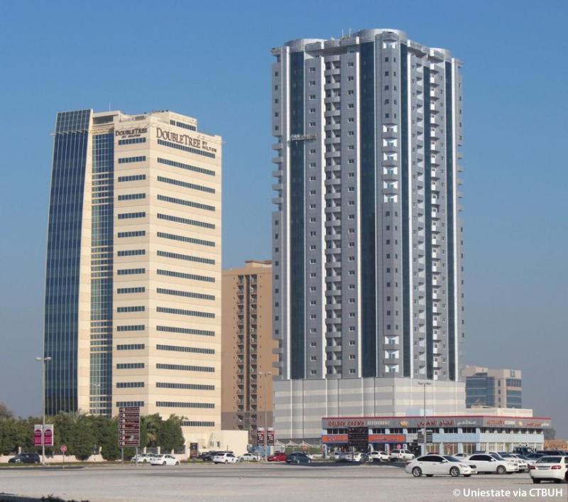 two tall buildings with cars parked in a parking lot at Your Comfort Starts Here in Ras al Khaimah