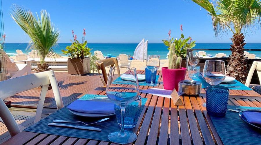 a wooden table with plates and wine glasses on the beach at Luxury Villa with Private Pool e Jacuzzi Year-Round a 25 min de Lisboa in Setúbal