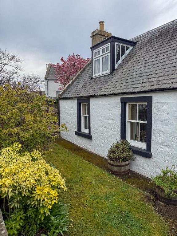 a white house with black windows and some flowers at Shop Cottage, Findhorn in Findhorn