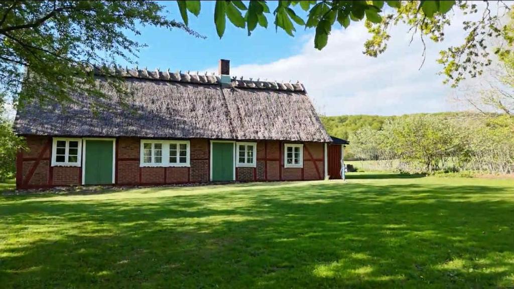 a red house with a thatched roof on a green lawn at Haqvins stuga in Förslöv