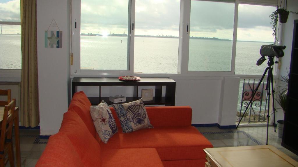 a living room with an orange couch in front of windows at Apartamento Mar Puerto Sherry in El Puerto de Santa María